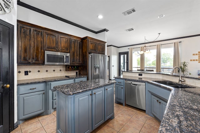 kitchen featuring appliances with stainless steel finishes, sink, dark brown cabinets, dark stone counters, and a kitchen island