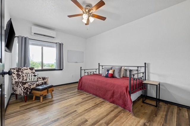 bedroom with hardwood / wood-style floors, ceiling fan, and a wall mounted air conditioner