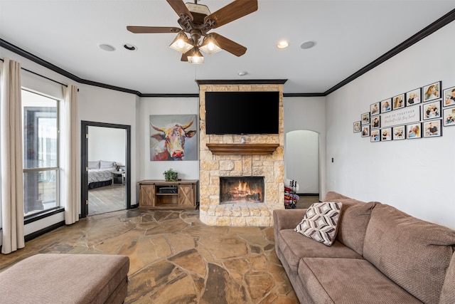 living room featuring a healthy amount of sunlight, ceiling fan, ornamental molding, and a stone fireplace