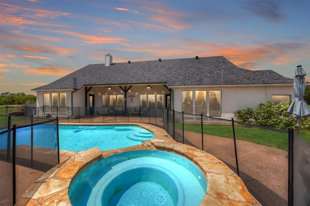 pool at dusk with an in ground hot tub and a patio area