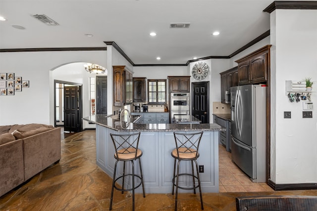 kitchen with light tile patterned floors, stainless steel appliances, sink, a breakfast bar area, and a center island with sink