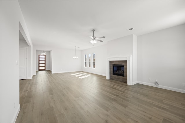 unfurnished living room with a fireplace, a healthy amount of sunlight, dark wood-type flooring, and ceiling fan with notable chandelier