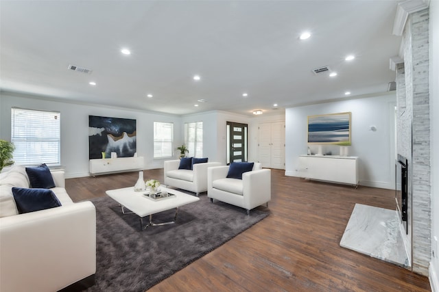 living room with ornamental molding, dark wood-type flooring, and a stone fireplace