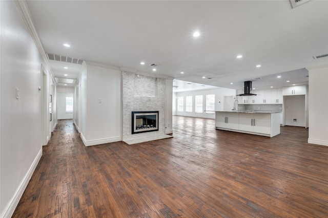 unfurnished living room with crown molding, a stone fireplace, dark hardwood / wood-style flooring, and a healthy amount of sunlight