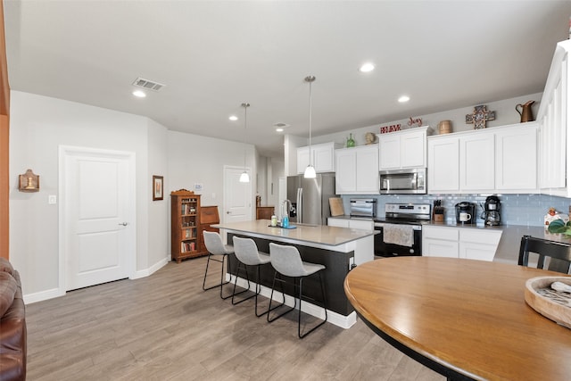 kitchen featuring backsplash, pendant lighting, a center island with sink, stainless steel appliances, and white cabinets