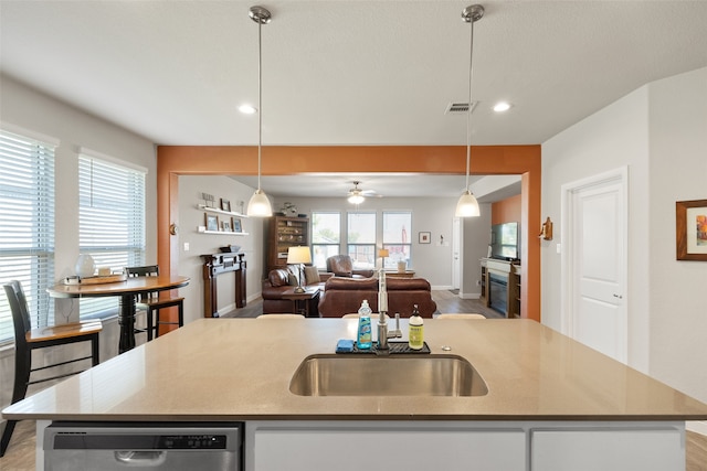 kitchen featuring ceiling fan, stainless steel dishwasher, a center island with sink, and decorative light fixtures