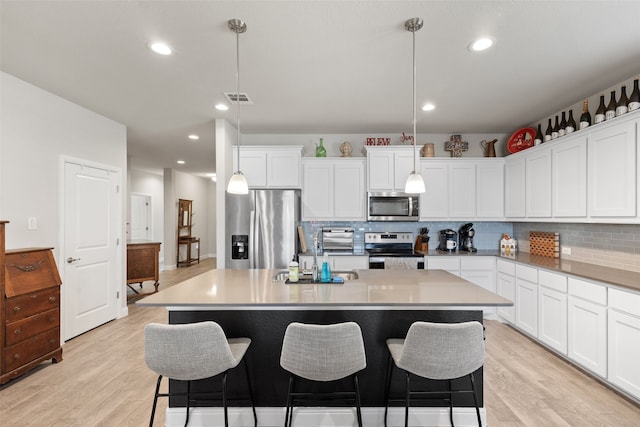 kitchen featuring appliances with stainless steel finishes, decorative light fixtures, white cabinets, and a kitchen island