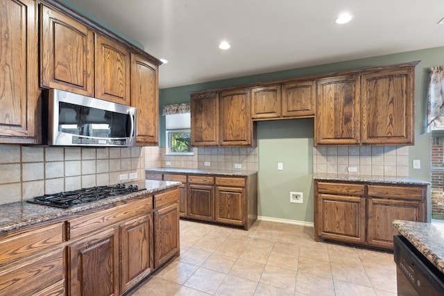 kitchen with light tile patterned floors, backsplash, dark stone counters, and black appliances