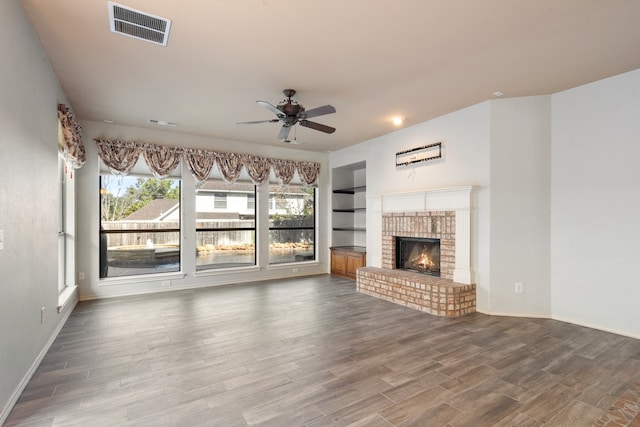 unfurnished living room featuring ceiling fan, hardwood / wood-style floors, built in shelves, and a brick fireplace