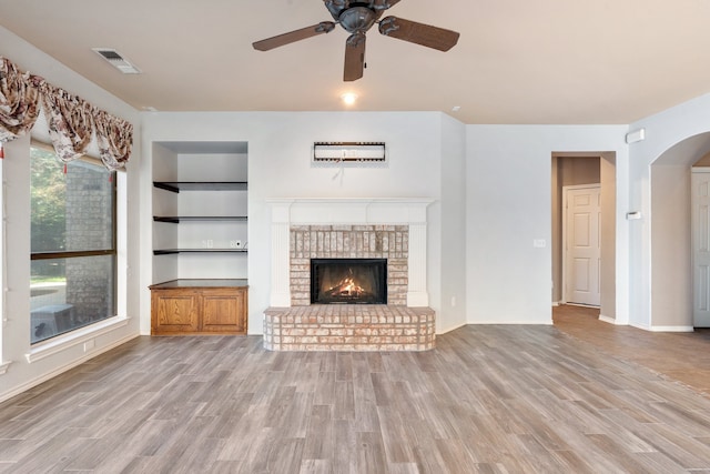 unfurnished living room featuring ceiling fan, a fireplace, built in shelves, and wood-type flooring