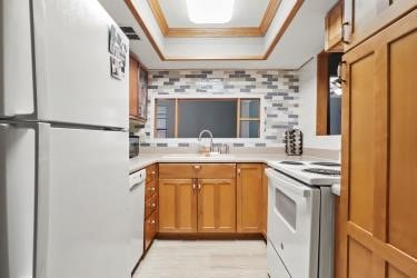 kitchen with light wood-type flooring, a raised ceiling, decorative backsplash, ornamental molding, and white appliances