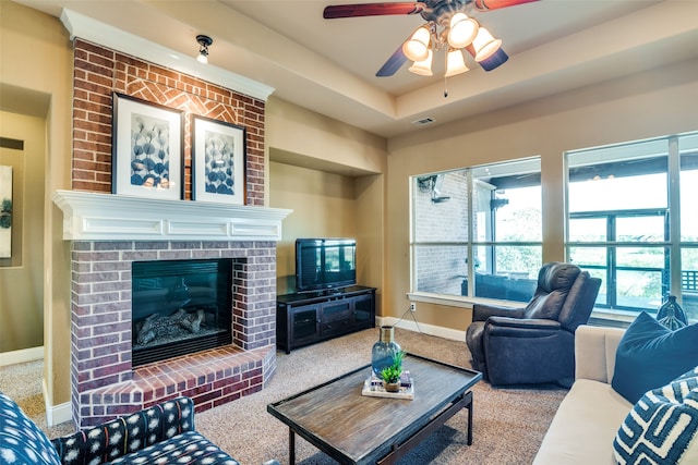 carpeted living room featuring a tray ceiling, ceiling fan, and a fireplace