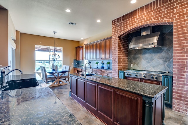 kitchen featuring wall chimney exhaust hood, hanging light fixtures, stainless steel gas cooktop, backsplash, and dark stone countertops