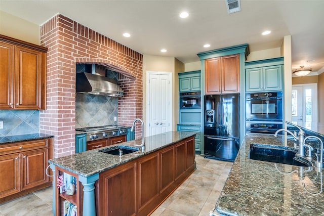 kitchen featuring decorative backsplash, a center island with sink, black appliances, and wall chimney range hood