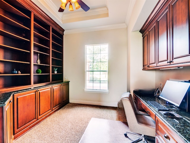 carpeted office featuring a tray ceiling, ceiling fan, built in desk, and ornamental molding