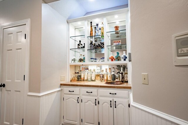 bar featuring tile counters and white cabinets