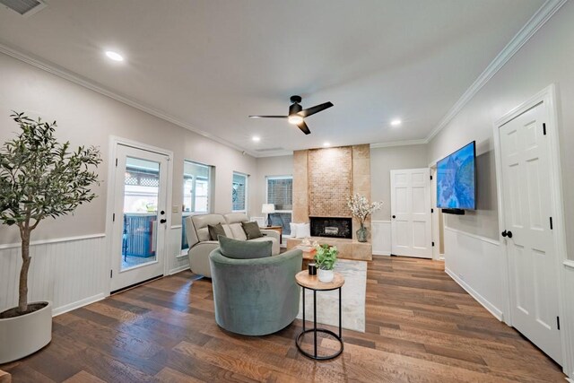 living room with brick wall, crown molding, a fireplace, dark wood-type flooring, and ceiling fan