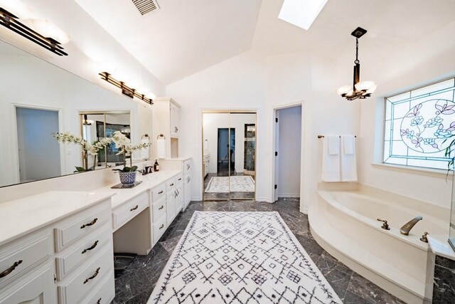 bathroom with vaulted ceiling with skylight, a bathing tub, tile patterned flooring, and vanity