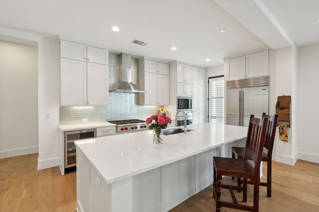 kitchen featuring beverage cooler, white cabinets, light countertops, wall chimney exhaust hood, and a center island with sink