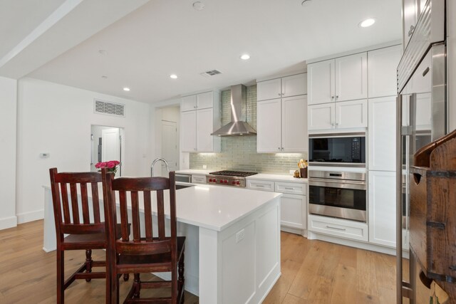 5270 Town And Country Blvd Unit 113, Frisco, TX 75034 - kitchen featuring white cabinets, light countertops, appliances with stainless steel finishes, wall chimney exhaust hood, and a center island with sink