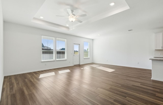 unfurnished living room featuring a raised ceiling, ceiling fan, and dark hardwood / wood-style flooring