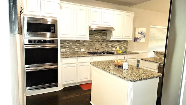 kitchen with appliances with stainless steel finishes, dark stone counters, white cabinetry, and range hood