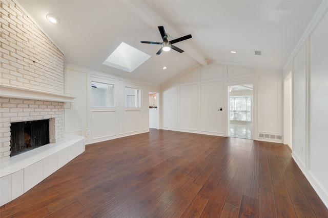 unfurnished living room featuring vaulted ceiling with skylight, dark hardwood / wood-style floors, brick wall, a fireplace, and ceiling fan