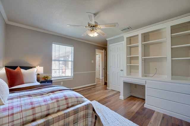 bedroom with a textured ceiling, built in desk, ornamental molding, hardwood / wood-style flooring, and ceiling fan