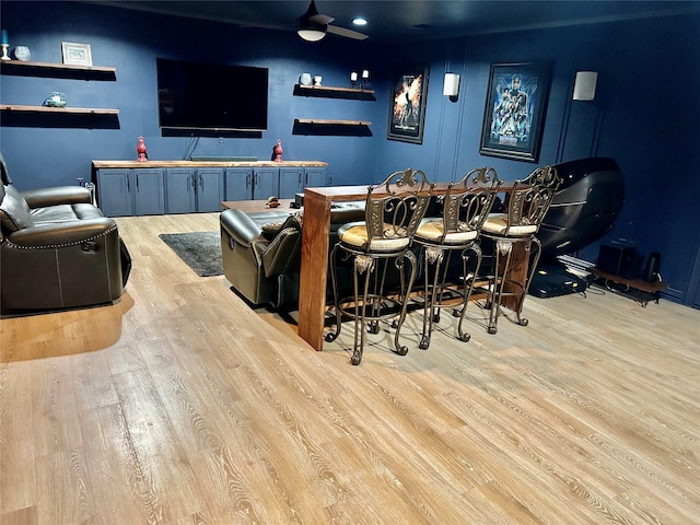 cinema with ceiling fan, bar, and light hardwood / wood-style flooring