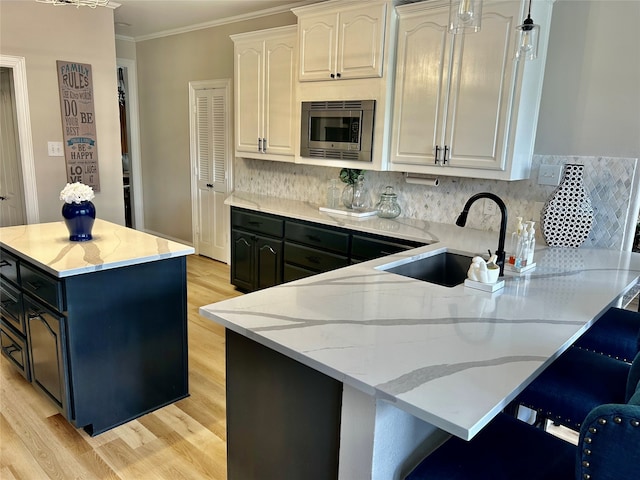 kitchen featuring stainless steel microwave, sink, light stone counters, white cabinets, and light wood-type flooring