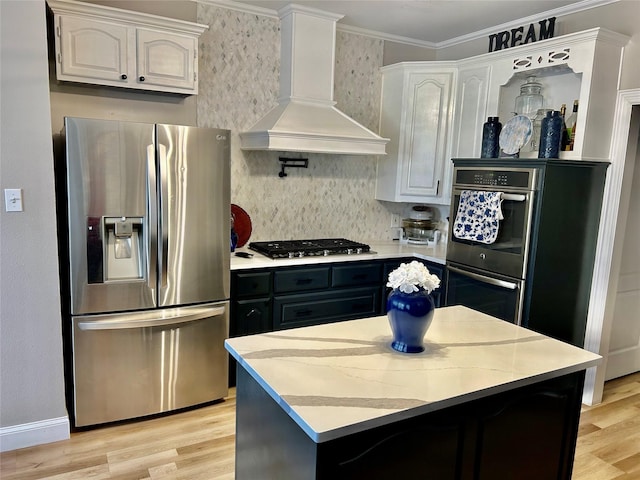 kitchen with appliances with stainless steel finishes, premium range hood, light wood-type flooring, a kitchen island, and white cabinets