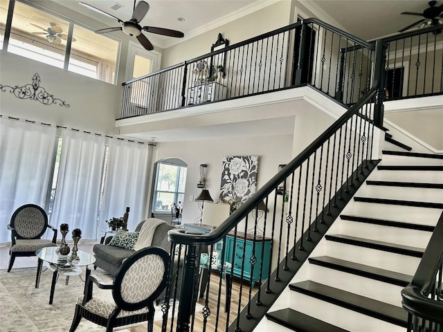 stairs with ceiling fan, ornamental molding, and a towering ceiling