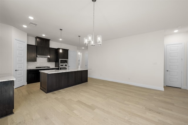 kitchen with decorative backsplash, an island with sink, a chandelier, light hardwood / wood-style flooring, and decorative light fixtures