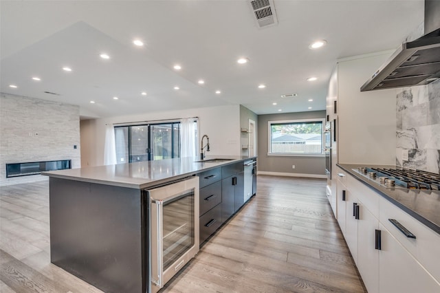 kitchen with white cabinetry, sink, wine cooler, a large island with sink, and wall chimney range hood