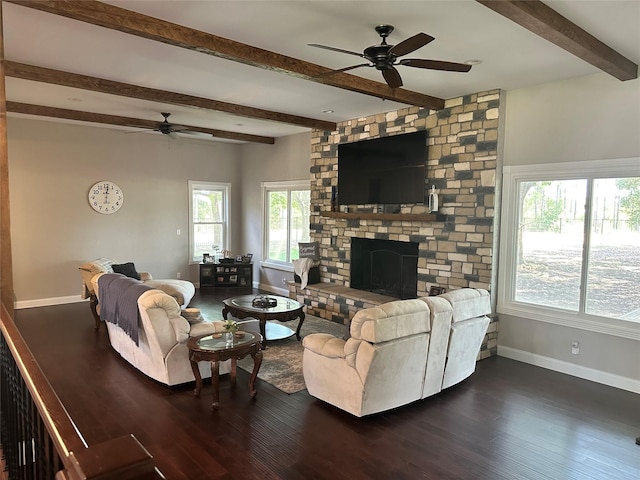 living room with ceiling fan, dark hardwood / wood-style flooring, a stone fireplace, and beamed ceiling