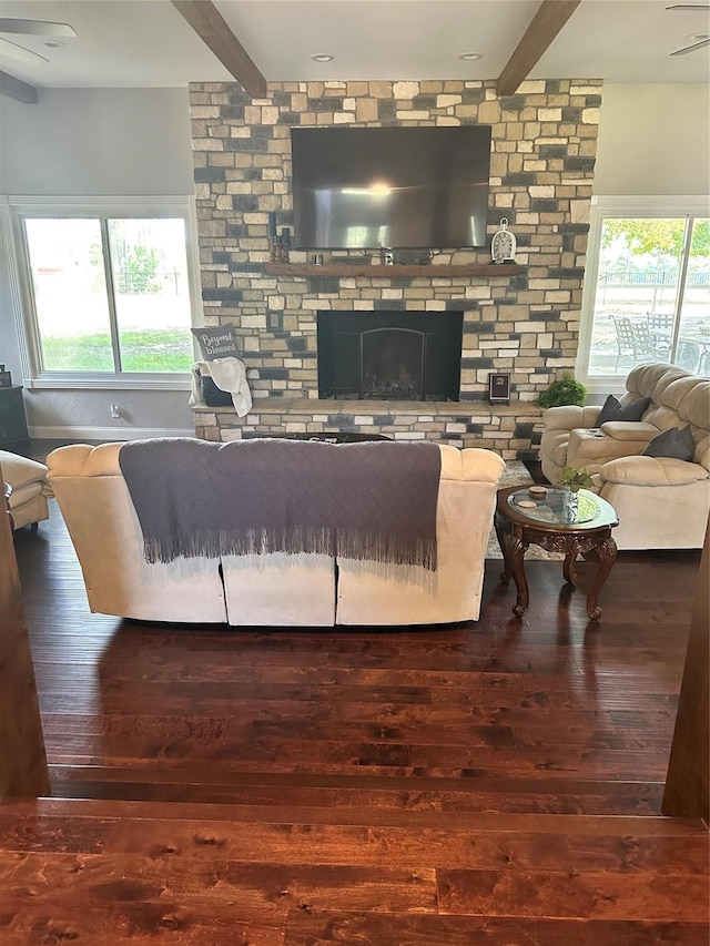 living room featuring ceiling fan, beam ceiling, hardwood / wood-style flooring, and a stone fireplace