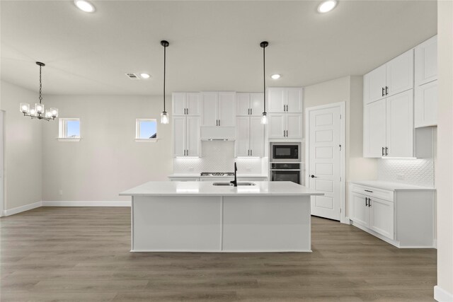 kitchen with white cabinets, hardwood / wood-style floors, a center island with sink, and oven