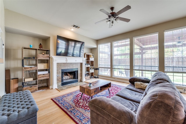 living room with a tiled fireplace, hardwood / wood-style floors, ceiling fan, and plenty of natural light