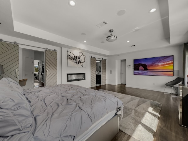 bedroom with hardwood / wood-style flooring, a raised ceiling, and a barn door