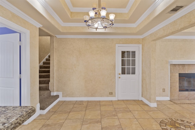 tiled foyer featuring a fireplace, ornamental molding, a raised ceiling, and an inviting chandelier