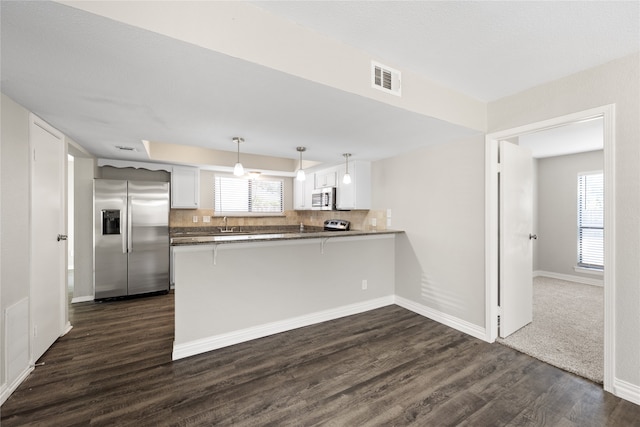 kitchen featuring kitchen peninsula, appliances with stainless steel finishes, decorative light fixtures, dark hardwood / wood-style flooring, and white cabinetry