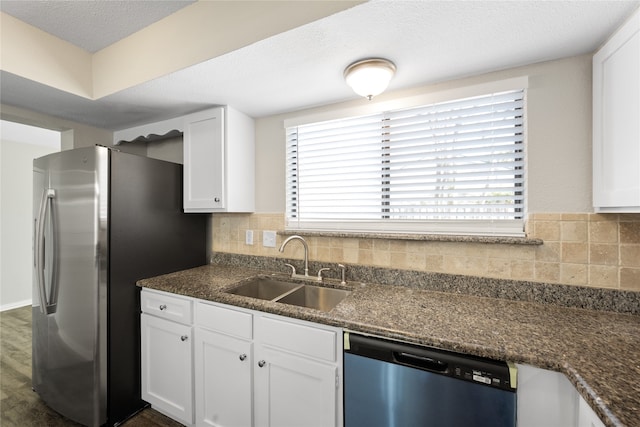 kitchen featuring appliances with stainless steel finishes, backsplash, dark stone counters, sink, and white cabinetry