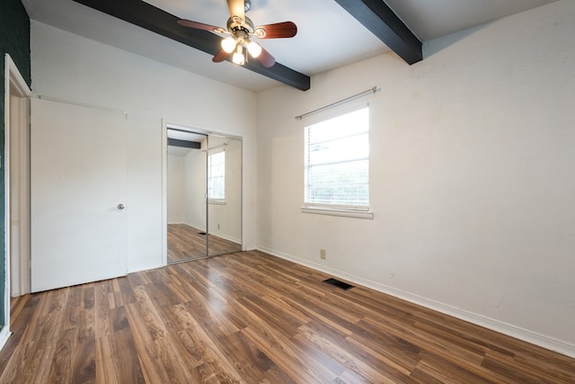 unfurnished bedroom with a closet, dark hardwood / wood-style floors, beamed ceiling, and ceiling fan