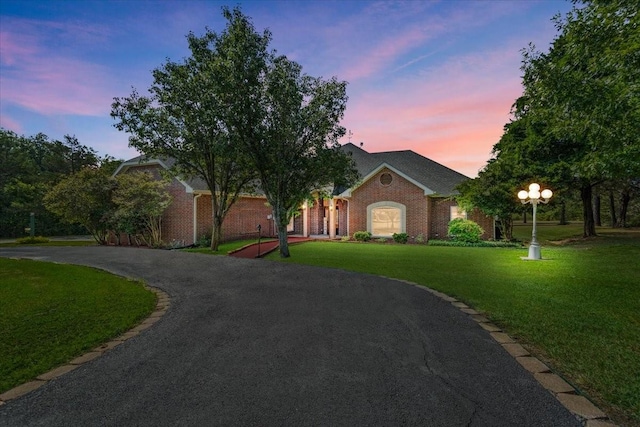 view of front facade with driveway, brick siding, and a yard