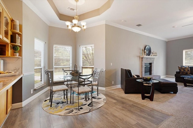 dining area featuring hardwood / wood-style floors, a raised ceiling, ornamental molding, a fireplace, and a notable chandelier