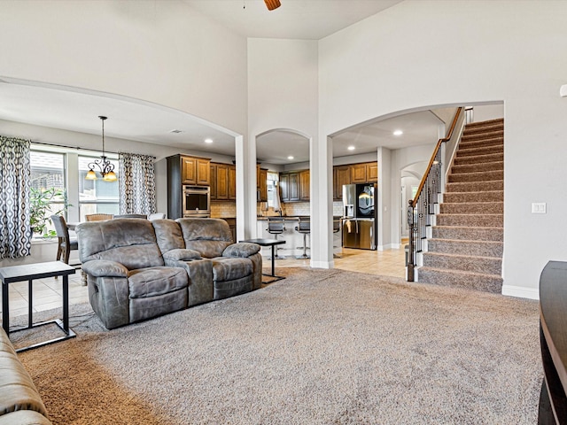 living room with light colored carpet, stairway, a high ceiling, baseboards, and ceiling fan with notable chandelier