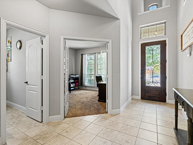 foyer entrance featuring light carpet, light tile patterned floors, a high ceiling, and baseboards