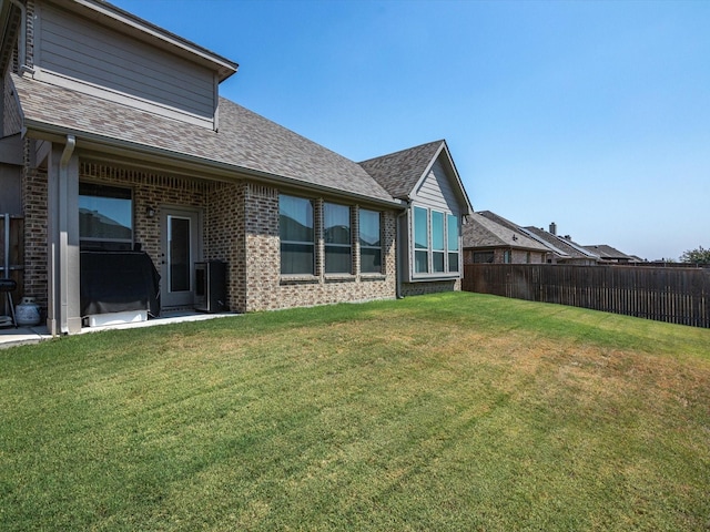 back of property with roof with shingles, brick siding, a lawn, and fence