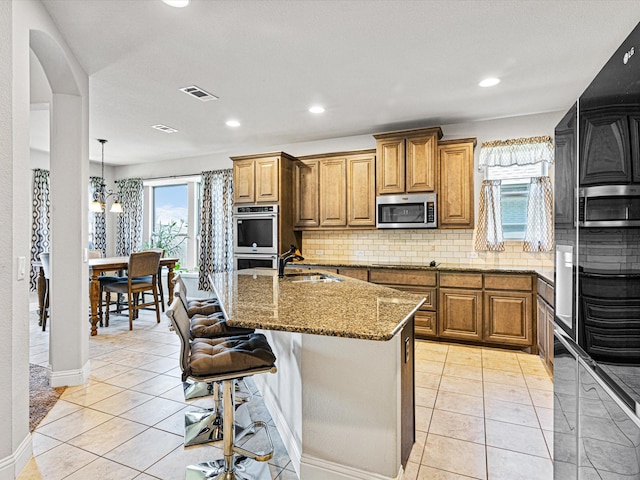 kitchen featuring stone countertops, stainless steel appliances, a sink, visible vents, and brown cabinets