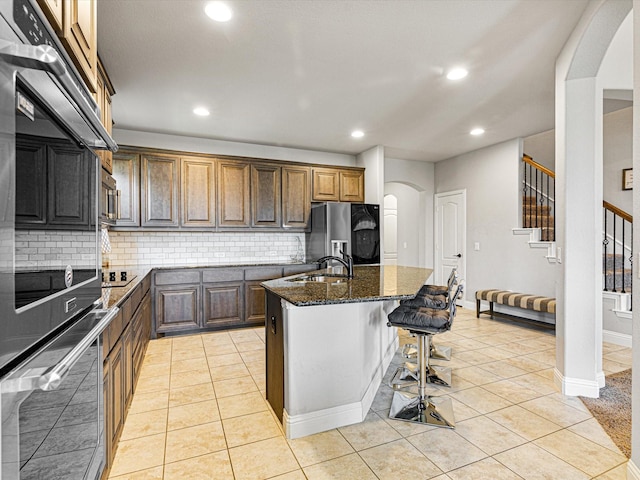 kitchen featuring arched walkways, a sink, appliances with stainless steel finishes, backsplash, and dark stone counters